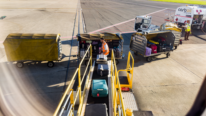 View from the window of a plane of suitcases being loaded onto an aircraft.
