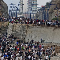 Large crowd of people gathered on a rocky beach and concrete embankment by the sea.
