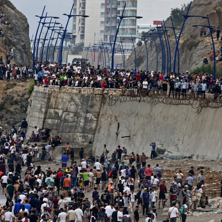 Large crowd of people gathered on a rocky beach and concrete embankment by the sea.