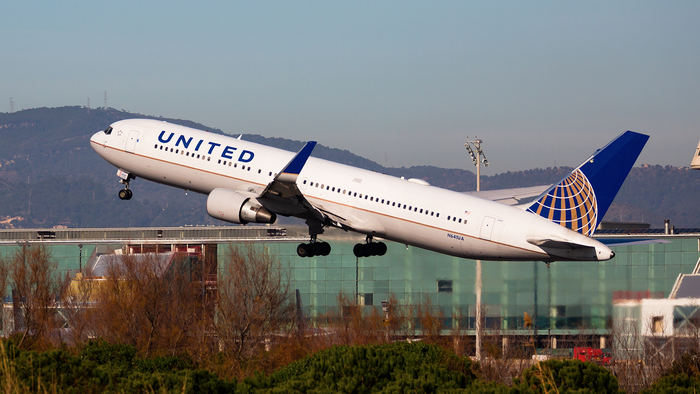 A United Airlines flight takes off in front of the Barcelona Airport building.