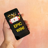 Man's hand holding a mobile phone with Epic win on screen from online casino
