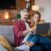 Mature couple sat on a sofa close, looking at a laptop