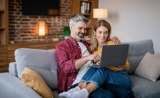 Mature couple sat on a sofa close, looking at a laptop