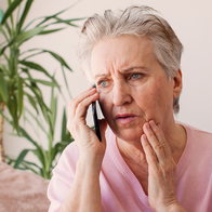 Older woman looking worried while holding a phone to her ear at home