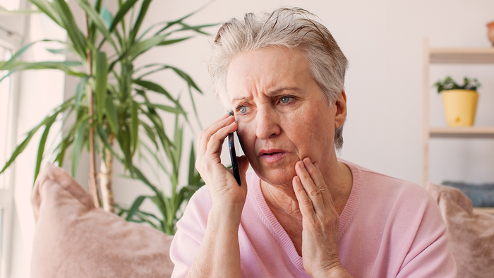Older woman looking worried while holding a phone to her ear at home