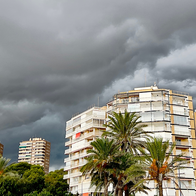 Storm clouds over Alicante with palm trees and apartment buildings in the foreground.