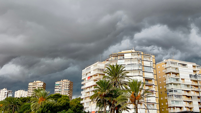 Storm clouds over Alicante with palm trees and apartment buildings in the foreground.