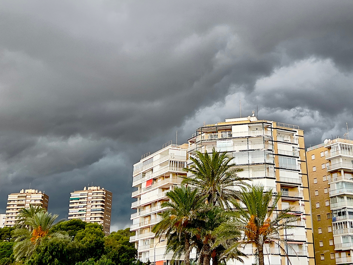 Storm clouds over Alicante with palm trees and apartment buildings in the foreground.
