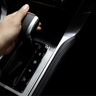 A hand shifts an automatic car gearstick into Drive.