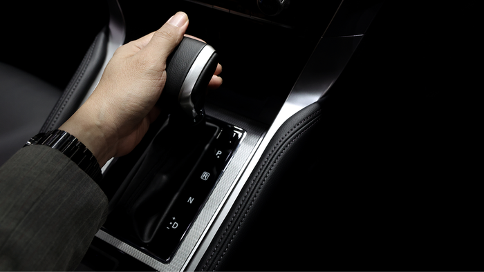 A hand shifts an automatic car gearstick into Drive.