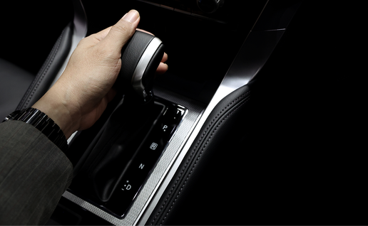 A hand shifts an automatic car gearstick into Drive.