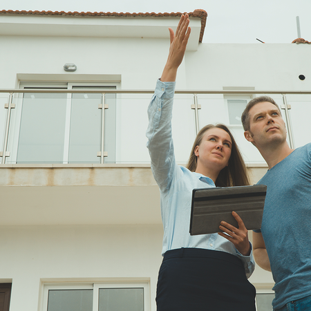 An estate agent showing a couple around a property, pointing out features of the building's exterior and balcony.