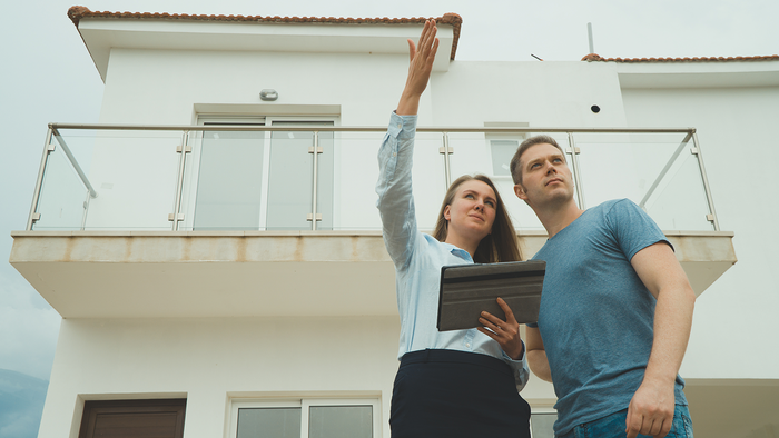 An estate agent showing a couple around a property, pointing out features of the building's exterior and balcony.