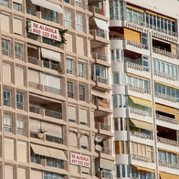 Row of apartment buildings in Costa Blanca, a few with "for rent" signs hanging on the façade.