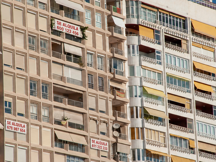 Row of apartment buildings in Costa Blanca, a few with "for rent" signs hanging on the façade.