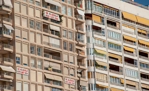 Row of apartment buildings in Costa Blanca, a few with "for rent" signs hanging on the façade.