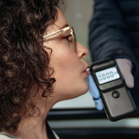 Woman takes a breathalyser test from her car as a traffic officer holds the breathalyser through the car window.