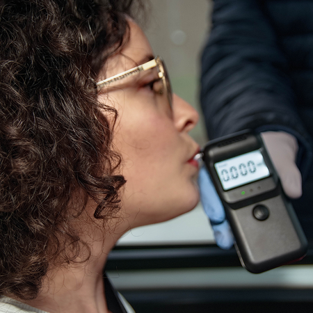 Woman takes a breathalyser test from her car as a traffic officer holds the breathalyser through the car window.