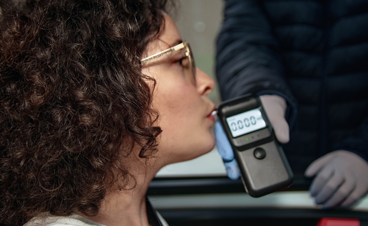 Woman takes a breathalyser test from her car as a traffic officer holds the breathalyser through the car window.