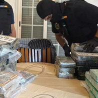 Two Aduanas customs officers in tactical vests sorting taped packages of cocaine on a table.
