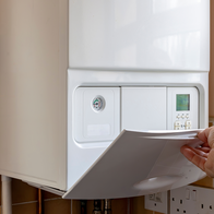 A person opens the control panel of a wall-mounted gas boiler in a kitchen.