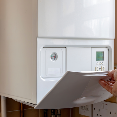 A person opens the control panel of a wall-mounted gas boiler in a kitchen.