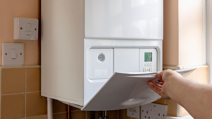 A person opens the control panel of a wall-mounted gas boiler in a kitchen.