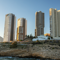 Two tall residential towers among Benidorm high-rises on a rocky headland, photographed at sunset.