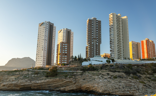 Two tall residential towers among Benidorm high-rises on a rocky headland, photographed at sunset.