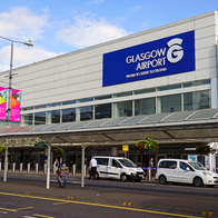 Exterior of Glasgow Airport's terminal building, with its illuminated sign, taxis and passengers at the entrance.