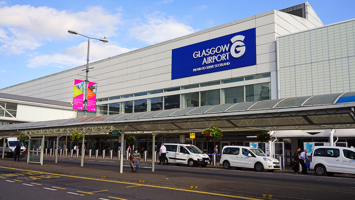 Exterior of Glasgow Airport's terminal building, with its illuminated sign, taxis and passengers at the entrance.