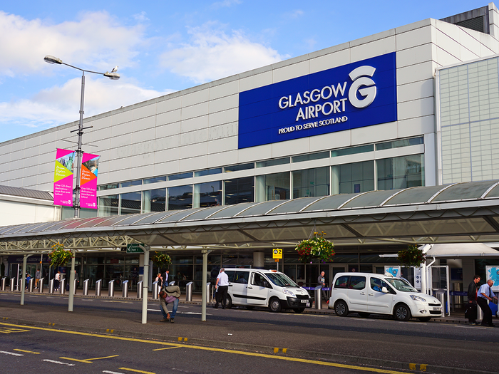 Exterior of Glasgow Airport's terminal building, with its illuminated sign, taxis and passengers at the entrance.