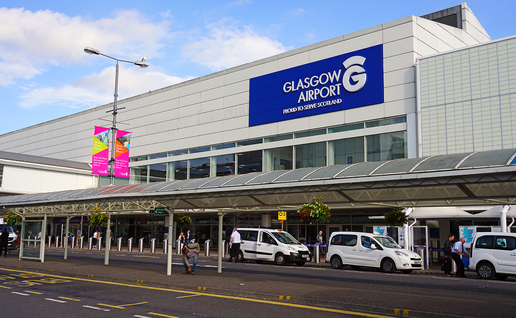 Exterior of Glasgow Airport's terminal building, with its illuminated sign, taxis and passengers at the entrance.