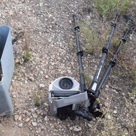 A damaged mobile speed camera and its tripod lying on gravel beside a road guardrail.