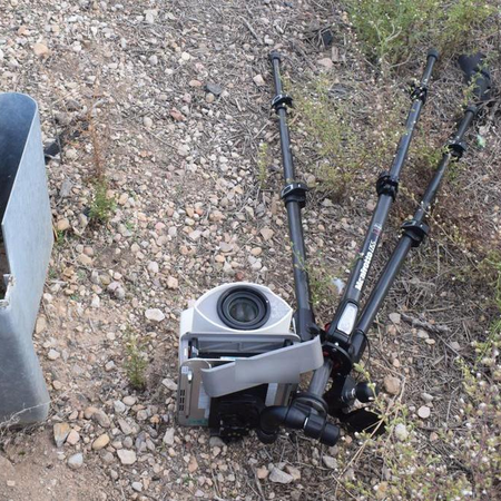A damaged mobile speed camera and its tripod lying on gravel beside a road guardrail.