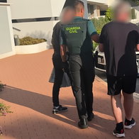 Guardia Civil officers escorting two people with blurred faces outside a residential building.