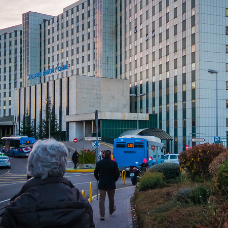 Exterior view of the Hospital Ramón y Cajal tower block in Madrid at dusk, with buses, cars and pedestrians outside the main entrance.