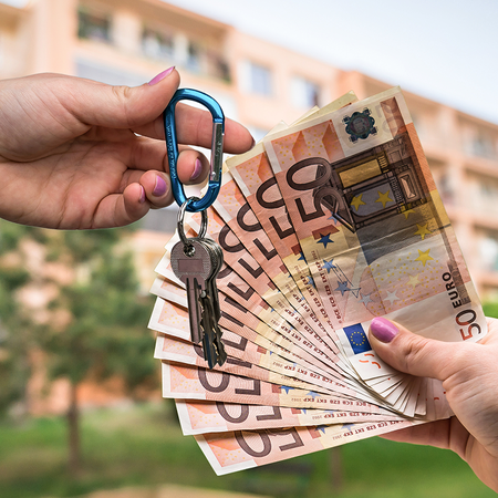 On person holding a set of keys as he exchanges it for another hand full of fifty euro notes, in front of a backdrop of Spanish apartment blocks.