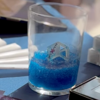 A NarXcup-branded ice cube stirrer sitting in a glass of blue, gelled drink, next to a stack of unused NarXcup ice cubes and branded promotional cards on a table.