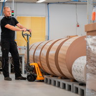 Male worker at Carccu with a hand pump forklift moving a palet with large rolls of paper