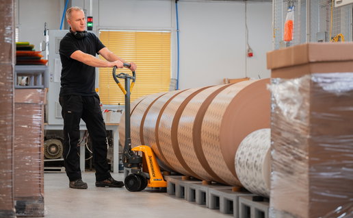 Male worker at Carccu with a hand pump forklift moving a palet with large rolls of paper