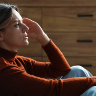 Woman sat on the floor resting on her sofa with her hand to her head looking frustrated.