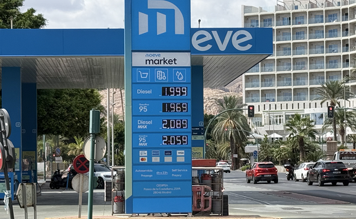 An electronic fuel price sign at a Moeve service station in Almería showing diesel and petrol prices per litre, with traffic and a hotel in the background.