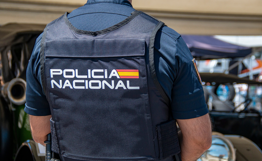 A Policía Nacional officer wearing a protective vest marked "Policía Nacional" stands with his back to the camera at an outdoor event.