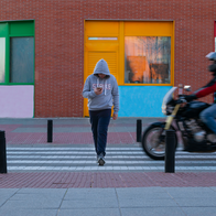 A man crossing a zebra crossing wearing a grey hoodie looking at his phone with a motorbike almost hitting him