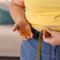 Woman in a yellow shirt measures her waist with a tape measure whilst holding slimming pills