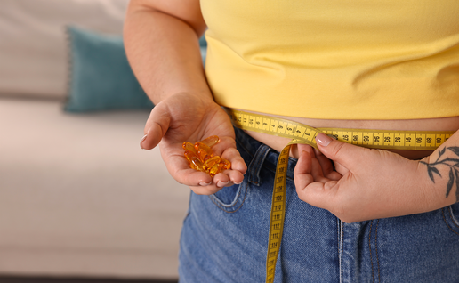 Woman in a yellow shirt measures her waist with a tape measure whilst holding slimming pills