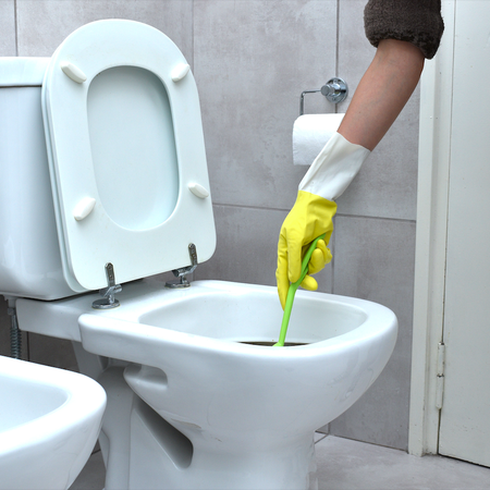 A woman with marigold gloves on scrubbing a toilet with a scrubbing brush