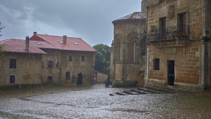 Rain pouring down on a an old stone street surrounded in large stone built houses