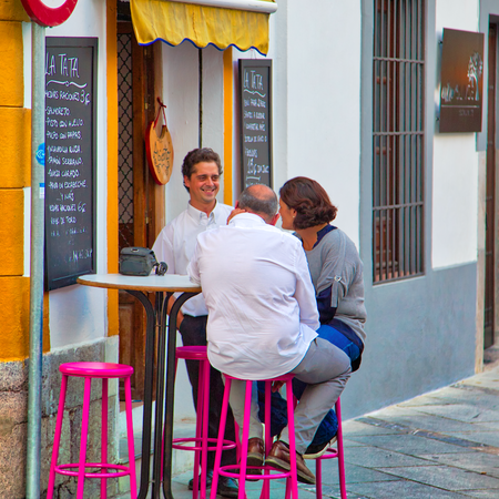 A couple talking to a waiter whilst sitting at a table outside a bar in Spain